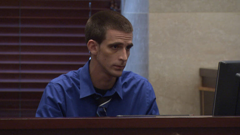 A man testifies in court wearing a blue shirt