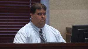 A man in a white shirt and tie testifies in court