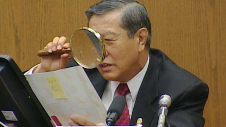Dr. Henry Lee looks through a magnifying glass at a piece of paper.