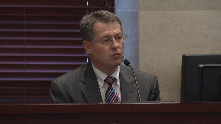 A man speaks into the microphone from the witness stand