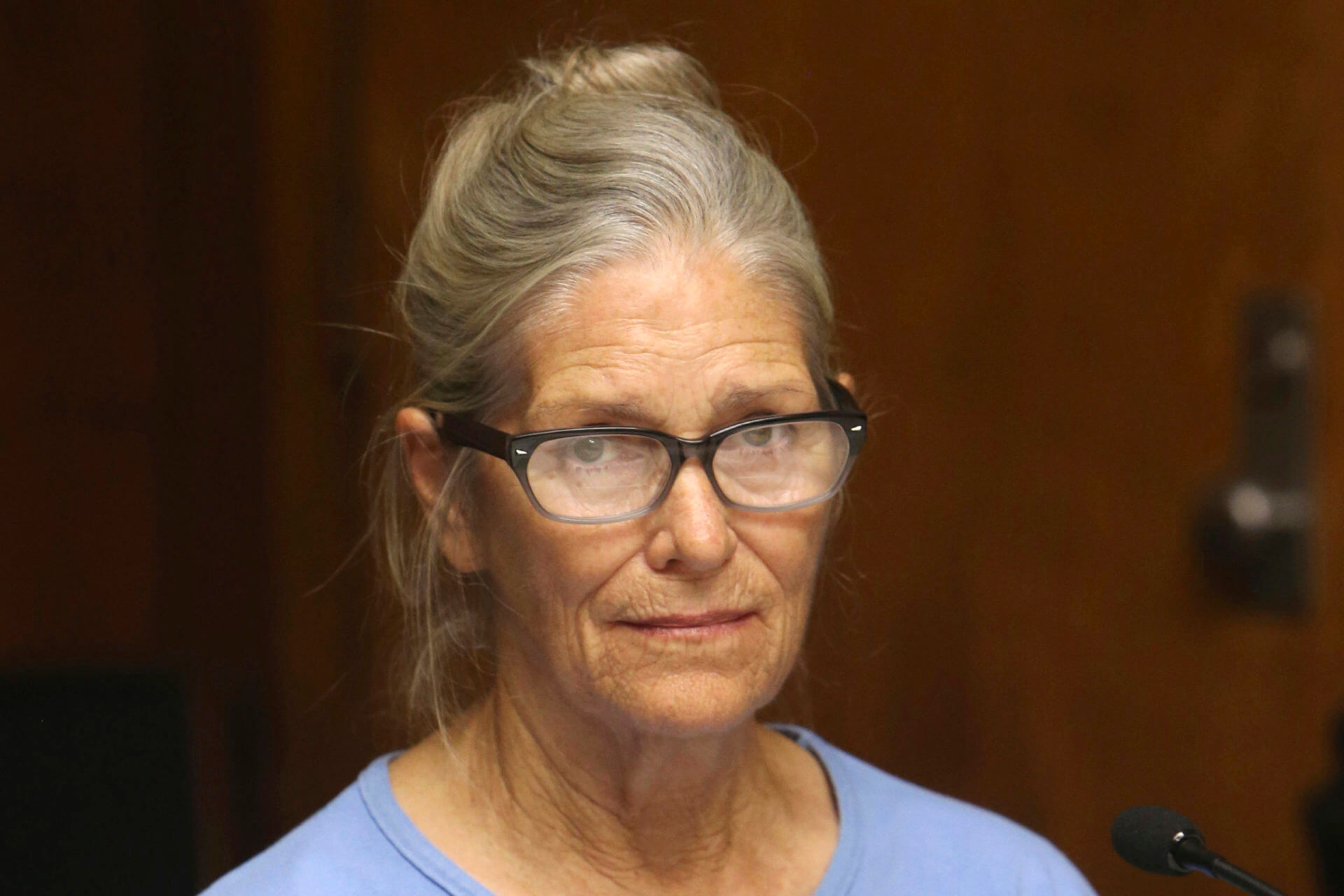 Leslie Van Houston, wearing glasses and a blue shirt, looks at the camera