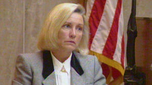 A woman sits in front of an American flag in court