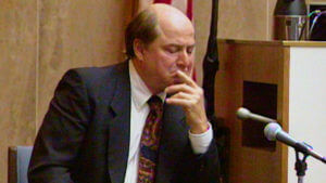 A man holds his head in his hand while testifying