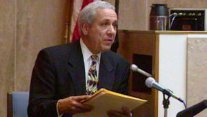 A man holds a legal pad while testifying