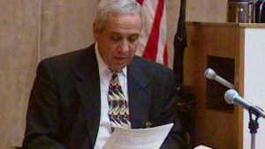 A man in a suit reads from a piece of paper