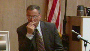 A man holds his hand to his face while testifying