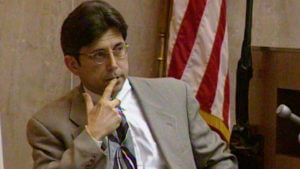 A man holds his hand to his face in court.