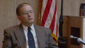 A man testifies in front of an American flag