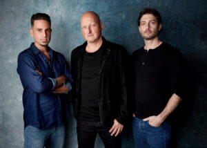 Three men stand in front of a blue background