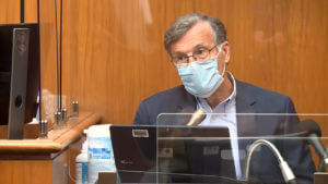 a man testifies wearing a mask