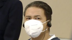 a man in a mask and wearing headphones looks at the camera in court