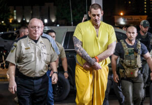 Casey White, in a yellow jump suit and shackles, walks flanked by police.