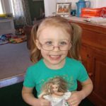 A little girl in glasses holds a doll