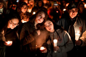 people holding candles gather in the dark at a vigil