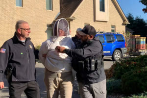 Rorie S. Woods, 55, of Hadley, Mass., center, wears a beekeeping suit while taken into custody by Hampden County Sheriff's Department officers, in Longmeadow, Mass., Wednesday, Oct. 12, 2022.