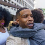 Tory Lanez walks out of a courthouse with a child around his neck