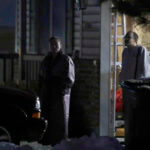 Neighbors watch as law enforcement officials work at a nearby Enoch, Utah, home where eight members of a family were found dead