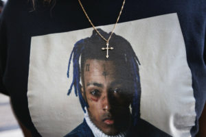 In this June 27, 2018, file photo a fan wears a cross around her neck dangling on a t-shirt in remembrance before she enters a memorial for the rapper, XXXTentacion in Sunrise, Fla.