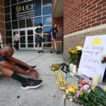 A person sits in front of the pop-up memorial for slain Spectrum News 13 journalist Dylan Lyons