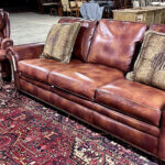 Brown leather sofa with striped throw pillows, matching arm chair and ottoman