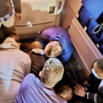 Passengers and crew restrain a man who tried to open a plane's emergency door and tried to stab a flight attendant.