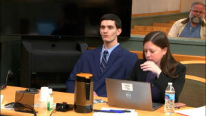 Zachary Latham and his attorney sit at a counsel table