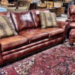 Photo of brown leather sofa with striped throw pillows, matching arm chair and ottoman