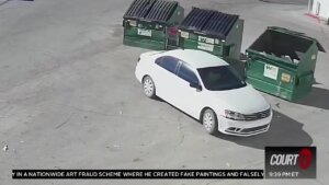 Still from surveillance video shows a white car next to green dumpsters