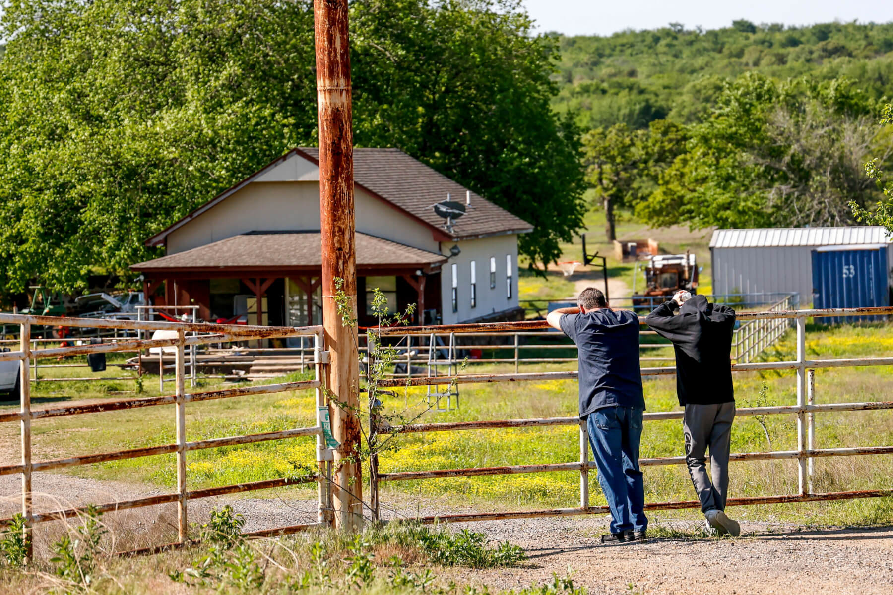 Two people stand at a fence with a building in the background