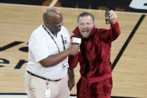 Conor McGregor stands on a basketball court with a man wearing white.