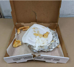 Open pizza box with paper plate, crumpled aluminum foil and pizza crusts.