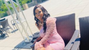 Carlee Russell appears cross-legged and smiling in a photo wearing a pink dress