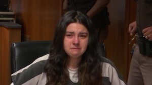 A woman, wearing a jail uniform, cries