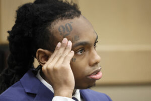 YNW Melly sits with his hand to his face in court.