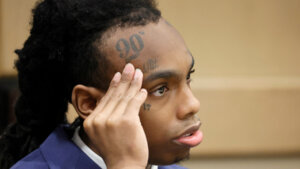 YNW Melly sits with his hand to his face in court.