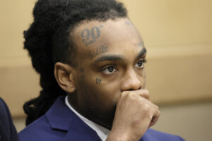 Jamell Demons, aka YNW Melly, sits in court with his hand to his face
