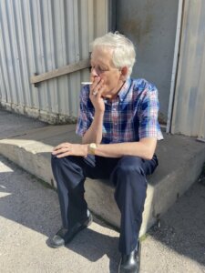 A man sits outside on a curb smoking a cigarette