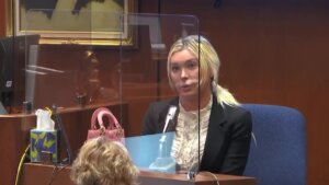 A woman sits behind plexiglass as she testifies in court