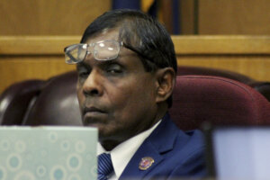 A man in a suit sits with glasses on his forehead.