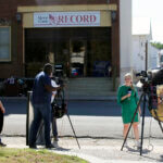 Television reporters and videographers report on the newspaper raid.