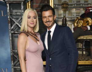 Katy Perry, wearing a pink dress, stands next to Orlando Bloom, wearing a suit.