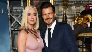 Katy Perry, wearing a pink dress, stands next to Orlando Bloom, wearing a suit.