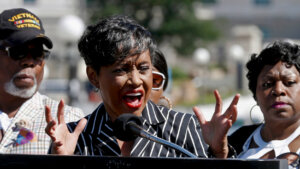 A woman speaks into a microphone at a podium outdoors