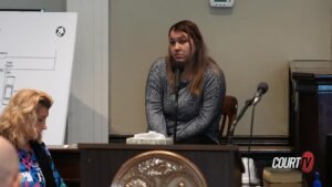 A woman sits in front a microphone testifying in court