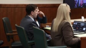 A man in a suit sits with two women at a table in court