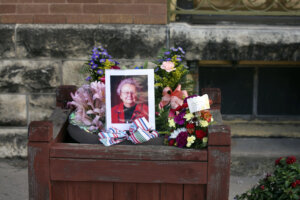 A photo of an elderly woman sits in a frame on a wooden bench surrounded by flowers