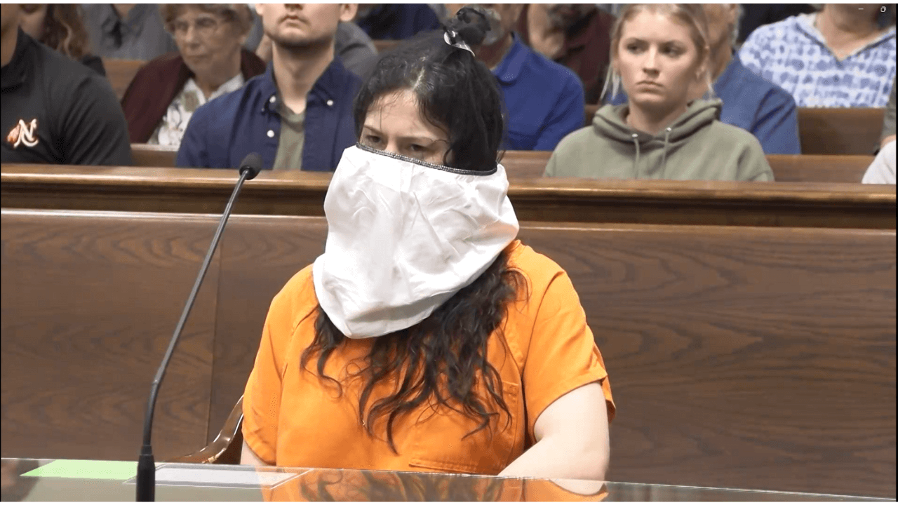 A woman sits in court wearing a spit hood