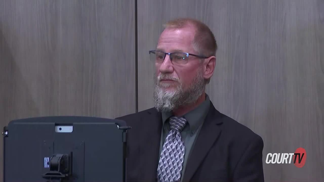 A man in a beard and suit sits in court