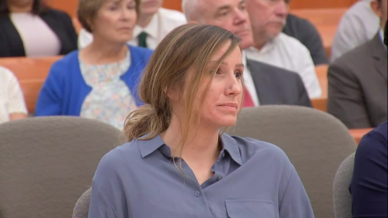 A woman in a blue shirt and hair in a messy bun sits in court