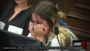 A young woman sits with her hands to her face